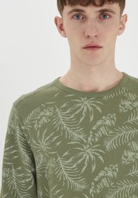 Sudadera de cuello redondo en verde oliva con un diseño texturizado de hojas en un tono más claro. Presenta costuras en los hombros y una tela suave.