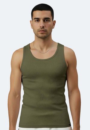 Uomo con capelli corti e scuri che indossa una canottiera a costine verde oliva e una collana a catena d'argento su uno sfondo chiaro e uniforme.
