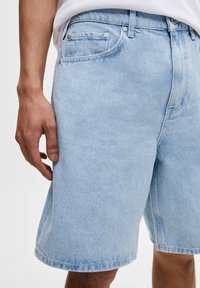 Svetle modré džíny šortky se střihem do rovna, vybavené pětivreckovým designem, viditelným šitím a kovovými akcenty.