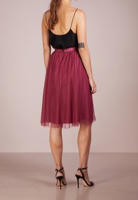 Burgundy tullekjol med prickar, åtstramad midja och svart satintopp. Har tunna band och svart sandaler med hög klack.