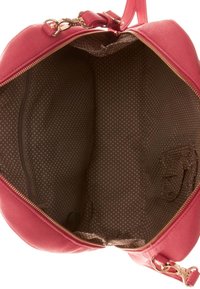 Borsa a tracolla rotonda di colore rosa con esterno texturizzato e dettagli in oro. L'interno presenta una fodera a pois marrone e una tasca con zip supplementare.