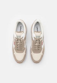 Sneakers beige e crema con tomaia in rete, dettagli in pelle scamosciata e suola in gomma marrone. Presentano lacci rotondi e logo Levi's sulla linguetta.