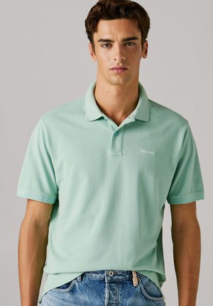 Mintgrønn poloskjorte laget av bomull, med klassisk krage, korte ermer og en diskret logo på brystet. Kombinert med blå denimjeans.