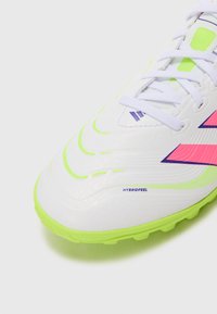 White soccer cleat with a textured upper, accented by bright green and pink details. Features a smooth toe cap and purple branding.
