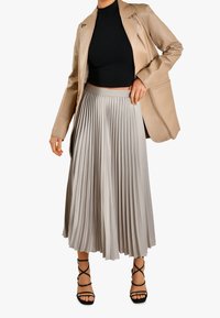 Plisowana szara spódnica midi z dopasowanym paskiem, zestawiona z czarną bluzką i beżową skórzaną marynarką. Całość dopełniają czarne sandały na paski.