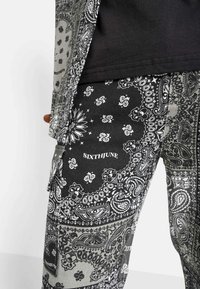 Zwart-witte gemarmerde broek met paisley ontwerpen, voorzien van een logo "SIXTHJUNE," gemaakt van stof met een gestructureerde afwerking.
