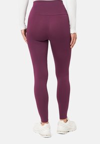 Legíny s vysokým pasem v hluboké švestkové barvě, vyrobené z elastického materiálu. Hladký povrch s minimálními švy, spárované s bílými sportovními botami.
