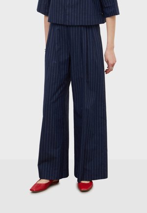 Pantalon large à rayures bleu marine associé à un haut assorti, porté avec des ballerines rouges pointues.