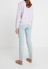 Sudadera de color lila claro, vaqueros en azul pálido, zapatos planos marrón claro. La sudadera tiene un cuello redondeado y puños acanalados.