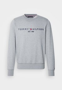 Sweat-shirt gris clair à manches longues avec col rond, avec le texte et le logo "Tommy Hilfiger Est. 1985" brodés sur la poitrine.