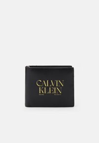 Black leather wallet with gold embossed "CALVIN KLEIN" logo. Compact rectangular shape with a stitched edge and zip closure.