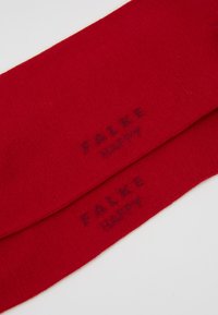 Rote Baumwollsocken mit glatter Textur, versehen mit den Marken "FALKE" und "HAPPY", die in einem dunkleren Rot nahe dem Bund eingewebt sind.