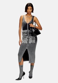 Gray ribbed dress with front zipper, patch pockets, and a mid-length cut. Worn with gray socks and black high heels, paired with a black handbag.