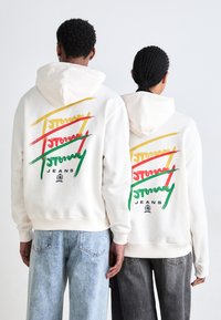 Sudadera blanca con capucha que presenta gráficos de texto multicolores en rojo, verde y amarillo en la parte posterior. Tejido de algodón suave, corte relajado.