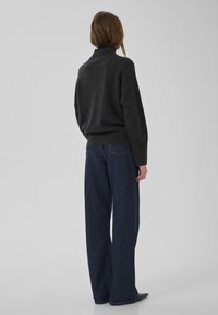 Tumši pelēks, rupji adīts džemperis ar augstu apkakli, kombinēts ar augsta vidukļa, platajiem ziliem džinsa biksēm. Vienkāršs, teksturēts dizains un piegriezums.