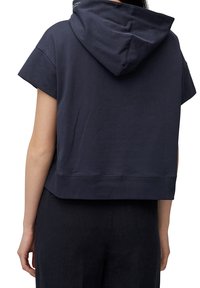 Sudadera de manga corta en color navy, confeccionada en tejido suave, con un corte holgado, capucha con cordón y ribete acanalado. Detalle de costura visible.