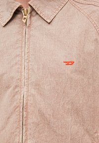 Απαλό ροζ σακάκι με φερμουάρ, κατασκευασμένο από υφή υφάσματος με ζαρωμένη όψη. Διαθέτει μυτερό γιακά και πορτοκαλί λογότυπο στο στήθος.