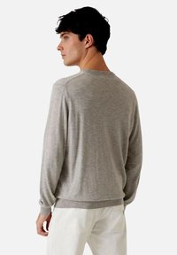 Suéter de punto gris claro con mangas largas y puños acanalados, presenta un escote redondo y un ajuste holgado. Textura suave con detalles mínimos.