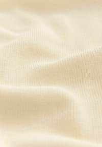 Gros plan sur un tissu couleur crème avec une texture lisse et douce, et un motif côtelé fin, mettant en valeur la légèreté du matériau.