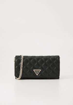 Pochette matelassée noire avec une bandoulière chaîne dorée et un logo triangulaire doré Guess au centre devant.