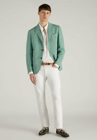 Lichtgroene linnen blazer met twee knopen, wit shirt, witte broek en zwarte schoenen met beige zolen, voorzien van een gestructureerde riem.