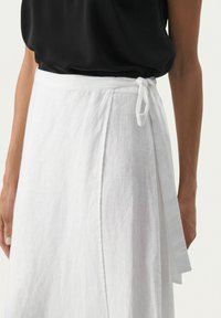 White linen wrap skirt with a tie closure at the waist, featuring a straight cut and subtle texture, paired with a black top.