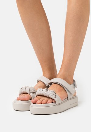 Jasnoszare sandały na platformie z marszczonym wierzchem i regulowanym paskiem na kostkę, z teksturowaną podeszwą zapewniającą przyczepność.