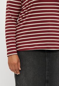 Burgunderstripet langermet topp med kremfarge horisontale linjer, som viser et mykt stoff og en avslappet passform. Svart denimskjørt synlig nedenfor.