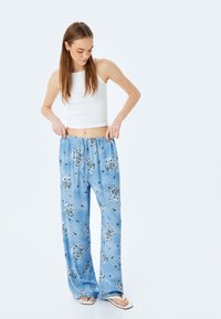 Un pantalon de pyjama bleu clair à motifs, avec une coupe ample et une taille élastique, associé à un débardeur blanc et des tongs.