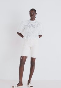 Valge puff-sleeve blouse lilleline tikand, vöökohaga ja beežide teksashortside ning valgete sandaalidega. Ükslane pind üle kogu toote.