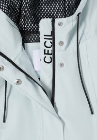 Veste gris clair avec doublure en maille noire, fermeture éclair noire, cordons de serrage noirs, boutons-pression argentés et "CECIL" imprimé près de la fermeture éclair.