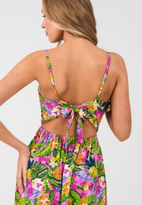 Květinové šaty s živým růžovým podkladem, zelenými listy a žlutými a bílými květinami. Mají tenká ramínka a detail na zavazování na zádech. Elastický pas.