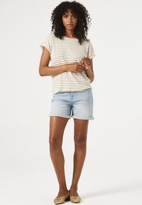 Haut à manches courtes rayé en crème et beige, associé à un short en denim bleu clair. Comprend des ourlets retournés et des ballerines plates.