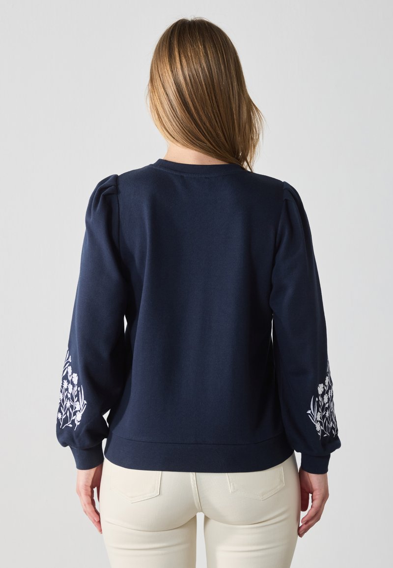Navyblauwe sweatshirt met pofmouwen, voorzien van witte bloemenborduursels op de manchetten. Zachte stof met een comfortabele pasvorm en ronde halslijn.