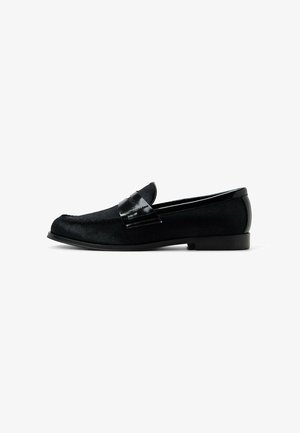 Schwarze Slipper mit einem strukturierten Stoff-Obermaterial und einem glänzenden Lacklederakzent auf dem Rist. Einfaches und elegantes Design mit flachem Absatz.