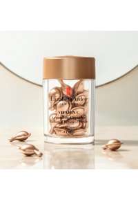 Genomskinlig cylindrisk behållare med ett lock i guld, innehållande mjuka, blekgula kapslar. Etiketterna inkluderar produktnamn och beskrivningar i svart text.