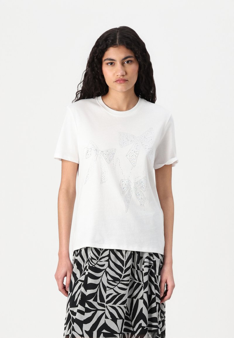 Vit bomull t-shirt med tre blanka, prydliga rosettmönster i olika storlekar. Tyget har en slät yta; korta ärmar är uppvikta.