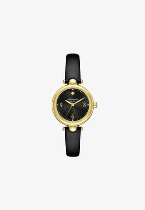 Reloj con correa de cuero negro, con una caja redonda en tono dorado, esfera negra, marcadores de hora dorados y un pequeño logo de trébol en la parte superior.