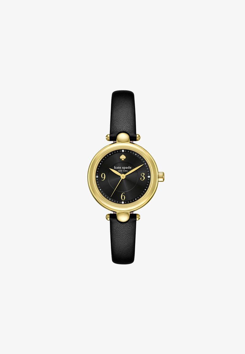 Reloj con correa de cuero negro, con una caja redonda en tono dorado, esfera negra, marcadores de hora dorados y un pequeño logo de trébol en la parte superior.