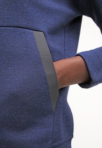 Mörkblå sweatshirt i texturerat tyg, med en slank svart sidficka och avslappnad passform. Långa ärmar, synliga sömnadsdetaljer.