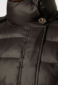 Czarna kurtka puchowa z wysokim kołnierzem i widocznymi przeszyciami. Wykonana z błyszczącego materiału, z zatrzaskami i suwakiem przy szyi.