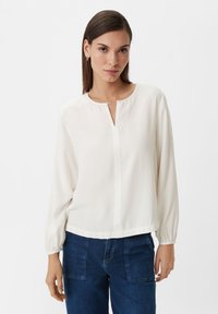 White, long-sleeve blouse with a round neckline and a short front slit. The fabric is smooth and slightly sheer, with gathered sleeves at the cuffs.