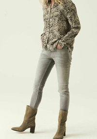 Hedvábná blůza s potiskem zvířecí srsti v béžové a černé; šedé skinny džíny; taupe semišové kotníkové boty na blokovém podpatku; těsný střih, dlouhé rukávy.