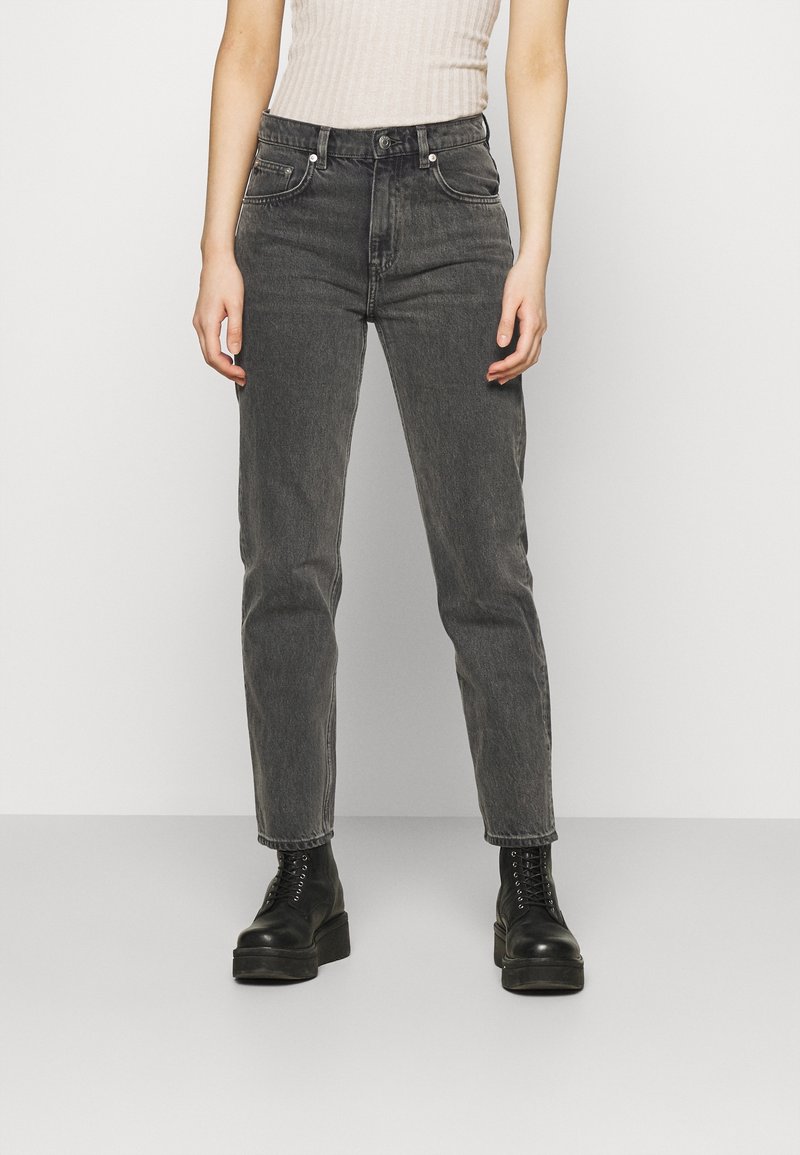 Jeans en denim gris foncé avec une coupe droite, design à cinq poches, couture visible et taille mi-haute, associés à des bottes noires.