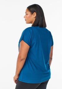 Teal tričko s krátkym rukávom a voľným strihom, okrúhlym výstrihom a hladkou textúrou, nosené s čiernymi nohavicami. Jednoduchý dizajn, bez vzorov alebo akcentov.