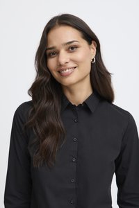 Fekete gombos ing gallérral, sima textúrával és finom fényességgel; fekete gombokkal az elején és szabott szabással.