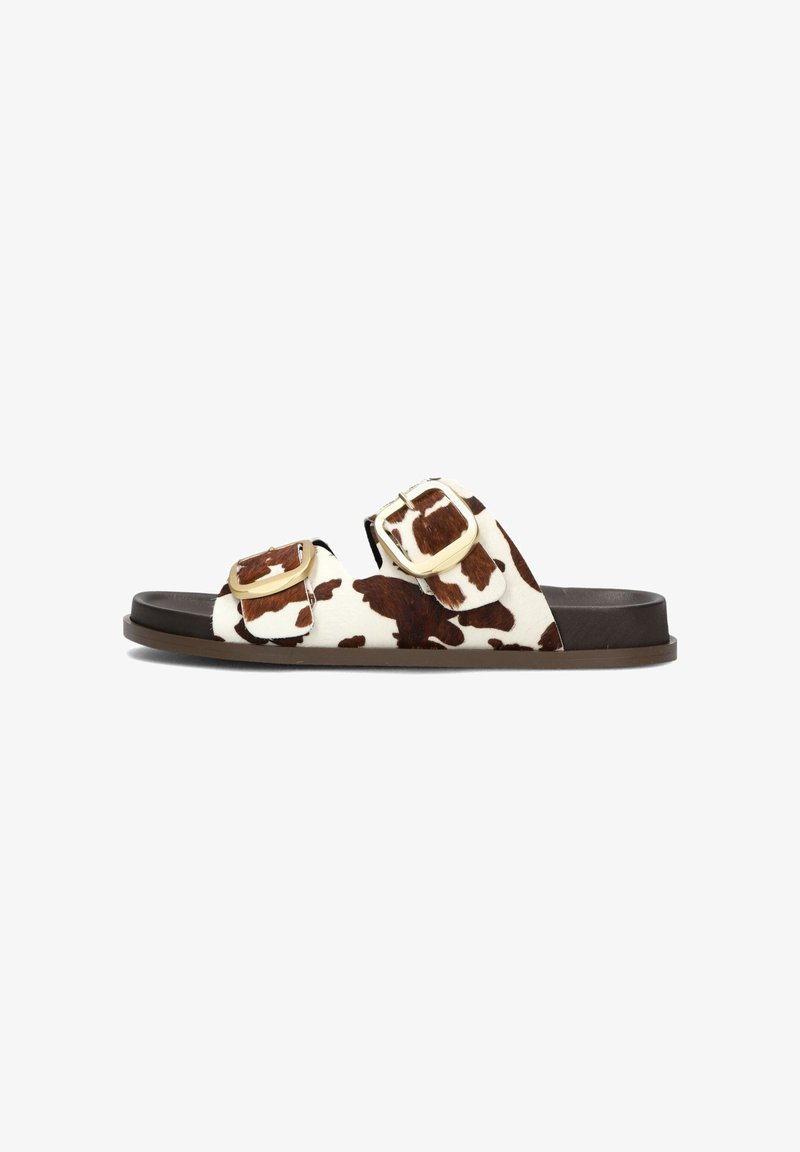 Bruine en witte cow-print slippers met twee verstelbare gouden gespen, een bruin textuur voetbed en een donkerbruine rubberen zool.