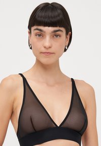 Black sheer bralette with a deep V-neck design, adjustable straps, and a wide underband. The material features a smooth texture.