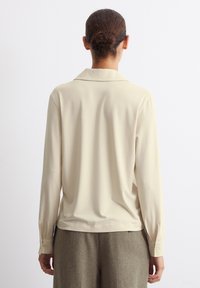 Langärmlige, cremefarbene Bluse mit einer weichen, glatten Textur und einem klassischen Kragen. Verfügt über geknöpfte Manschetten und eine lässige Passform.