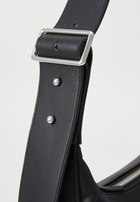 Cinghia a spalla in pelle nera con fibbia rettangolare in argento, rivetti decorativi in argento e una superficie liscia con una leggera lucentezza.